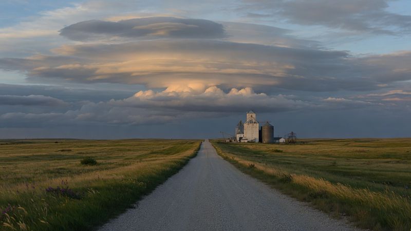 Gravel road across a South Dakota prairie toward a grain elevator.